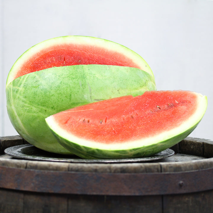 A cut Refined Sugar Watermelon on top of a barrel against a light background.