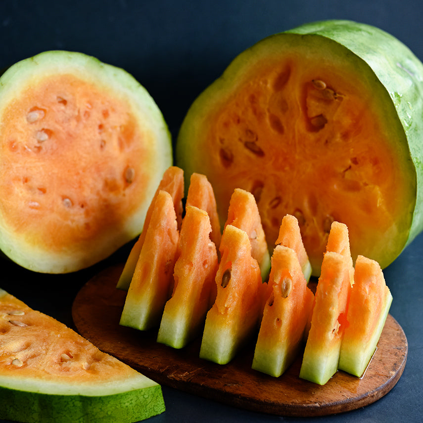 Sliced and cut Texas Golden Watermelon on a wooden cutting board on dark blue background.