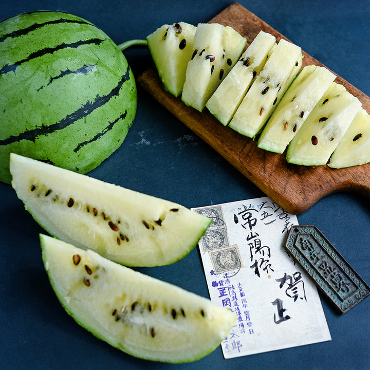 Sliced Silver Yamato Watermelon with a postcard from Japan on a jade background.