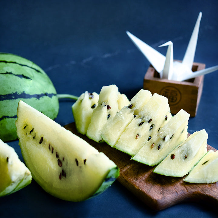 Silver Yamato Watermelon sliced with a paper crane on a dark blue background.