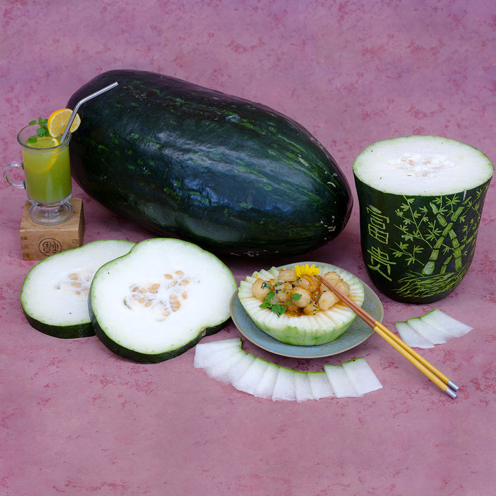 An arrangement with a whole and carved Giant Bullet Head Wax Melon, drink and entree on a pink background.