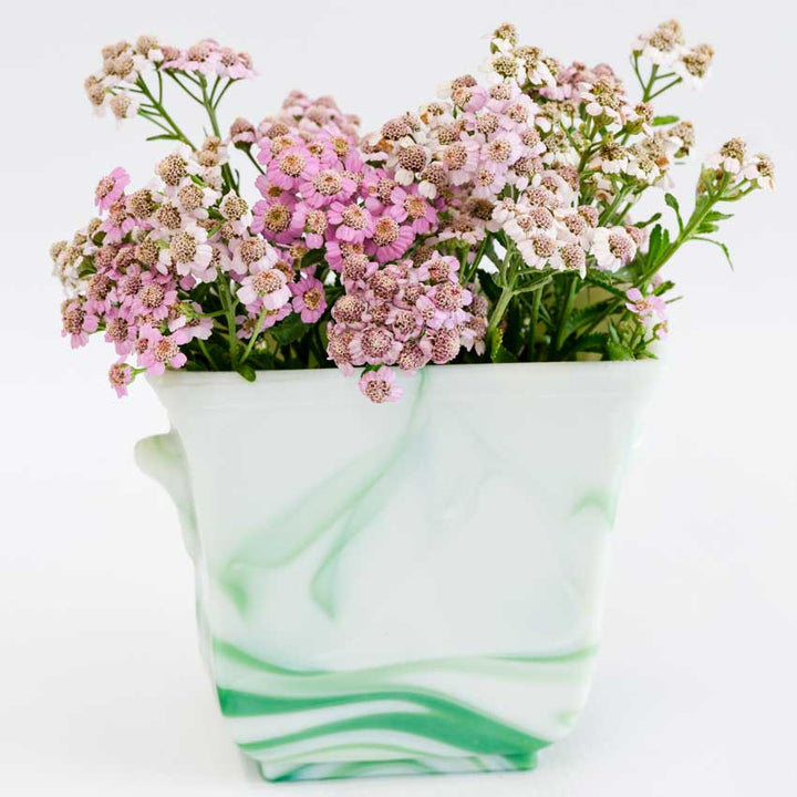 Love Parade Yarrow blooms in a green and white marble vase on a white background.