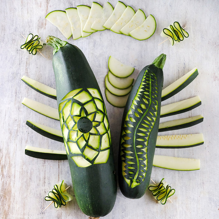 Black Beauty Zucchini Summer Squash carved and sliced on a white washed wood background.