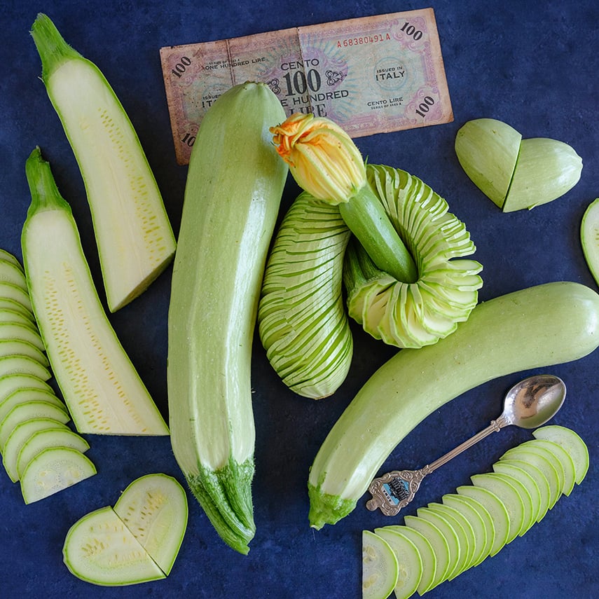 Spiral sliced and regular Long White of Palermo Zucchinis on a wood board with blue background.