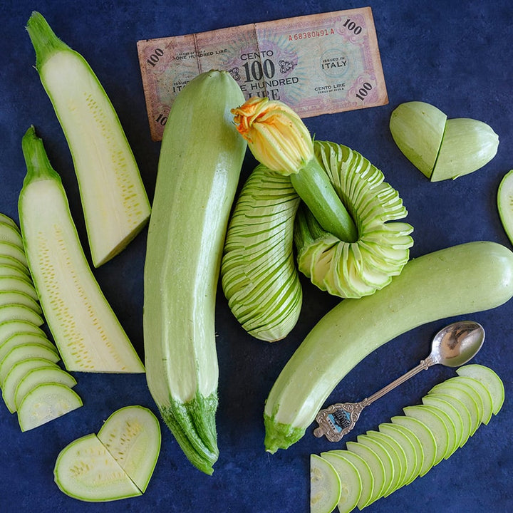 Spiral sliced and regular Long White of Palermo Zucchinis on a wood board with blue background.