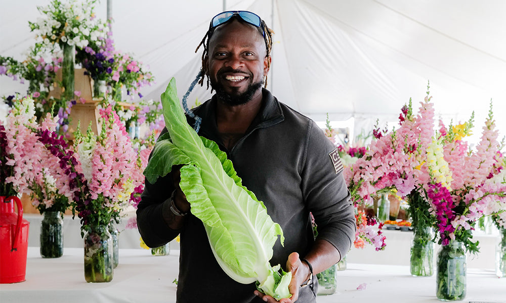 A grower holding a napa cabbage among cut flowers at a spring garden festival