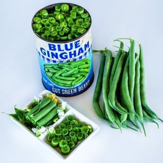 Cut and whole Blue Lake Bush 274 Beans in a dish with a can of beans on white background.