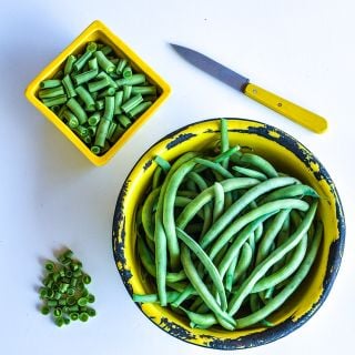 Cut and whole Contender Beans in a yellow rustic bowl and ayellow dish with a yellow handled knife.
