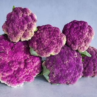 A half dozen Purple of Sicily Cauliflower heads stacked on a table.