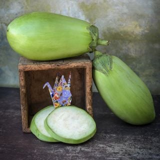 Shiromaru Eggplant sitting atop a wooden box with slices down below.