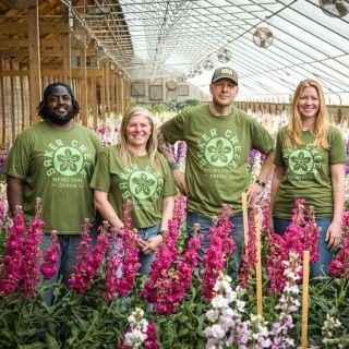 Baker Creek staff shows off Baker Creek Herb-colored T-Shirts in a greenhouse full of stock.