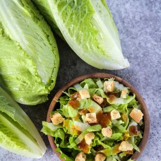 Three Crisp Mint Lettuce heads and a bowl of salad on a stone background.