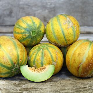 Ha'Ogen Melons stacked up with a melon slice on a wooden background.