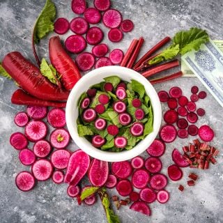 Cut and whole Red Beauty Radishes surrounding a radish green salad with money on a gray background.