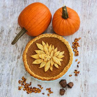 A pumpkin pie with two New England Sugar Pie Pumpkin Winter Squash with seeds on a light background.