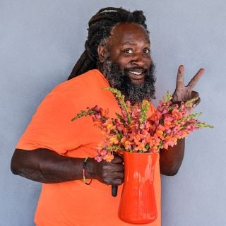 A smiling Baker Creek horticulturalist wearing an orange shirt holding an pitcher full of Orange Wonder Snapdragons.