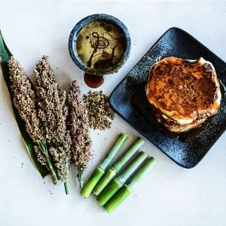 Mennonite Sorghum seed heads and canes with pancakes and sorghum syrup on linen background.