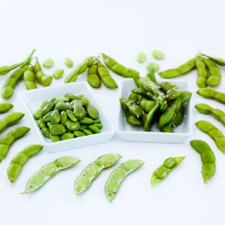 Cooked Tankuro Soybeans in a couple small dishes surrounded by more soybans on a white background.