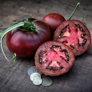 Cut and whole Black from Tula Tomatoes with coins on wood background.