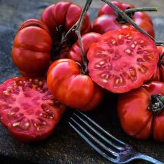 A cluster of Costoluto Genovese Tomatoes with one sliced on dark wooden cutting board with a fork.