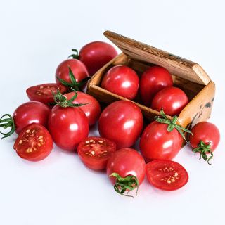 Cut and whole German Lunchbox Tomatoes in and surrounding a wooden box from Germany on white.