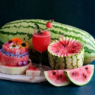Jubilee Watermelon whole and sliced with juice and watermelon cake on dark blue background.