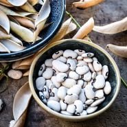 A bowl of Alabama Blackeyed Butterbean Lima Beans with hulls in anotherbowl on a wooden background.