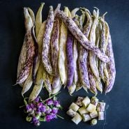 Dragon Tongue Beans with a pile of pink blooms and another pile of cut beans on a dark background.
