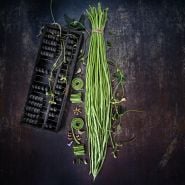 Bundled, chopped and whole Taiwan Yard-Long Beans with blooms on a dark brown background.