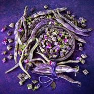 Cut and whole Dragon Tongue Beans arranged on a dark purple background.