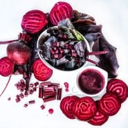 A salad made from beet greens surrounded by sliced Bull's Blood Beets and juice on a white background.