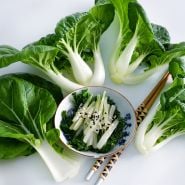 Baby Milk Bok Choy arranged around a bowl of sauteed leaves and stems on a white background.