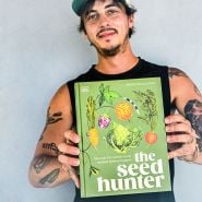 Author Mitch McCulloch holds out his book, The Seed Hunter, aaginst a grey wall.