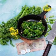 Cooked Natalina Di Fasano Cima Grande Broccoli Rabe in a cast iron skillet surrounded with fresh rabe.