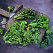 Cooked and fresh Natalina Di Fasano Cima Grande Broccoli Rabe on a wooden cutting board.