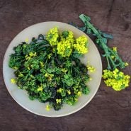 Cooked Rapini with blooms on a plate sitting on a vintage woodenbackground.