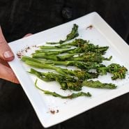 A man holding a grilled plate of gourmet Rapini.