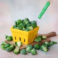 A yellow ceramic basket full of Long Island Improved Brussels Sprouts with a green handled knife.