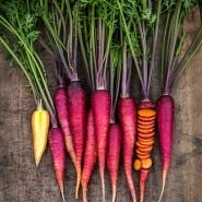 Cut, sliced and whole Purple Dragon Carrots on a wooden board.