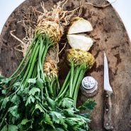 Overhead view of Giant Prague Celeriac heads on a wooden cutting board with a knife and salt shaker.