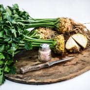 Several whole and cut heads of Giant Prague Celeriac with a salt shaker and knife on wooden cutting board.