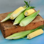 Damaun KS Super Sweet Corn with and without husks on a wood box against a blue background.
