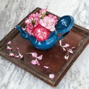 An arrangement of Raspberry Ripple Dianthus in blue tea pot on wooden tray.