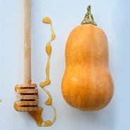 A single Honeynut Butternut Winter Squash with a honey dripper on a light background.