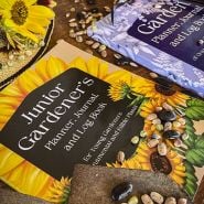 An adult garden planner alongside a Junior Gardener's planner booklet with gardening tools and scattered seeds.