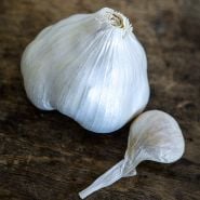 A macro view of a single bulb and clove of Chet's Italian Garlic on a wooden background