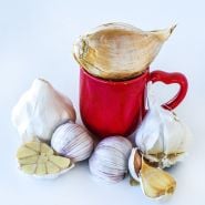 Garlic cloves and bulbs in the Garlic Lover Sampler Pack arranged around a red mug with a heart on the handle.