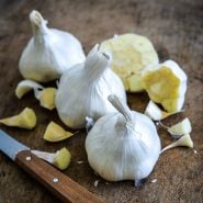 A trio of whole Inchelium Red Garlic bulbs with a cut bulb and cloves on wood.
