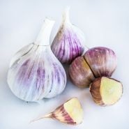 A close-up of pink hued Leningrad Garlic bulbs and cloves on a white background.