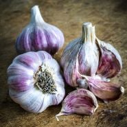 A close-up view of Vietnamese Red Garlic bulbs and cloves on a wooden cutting board.